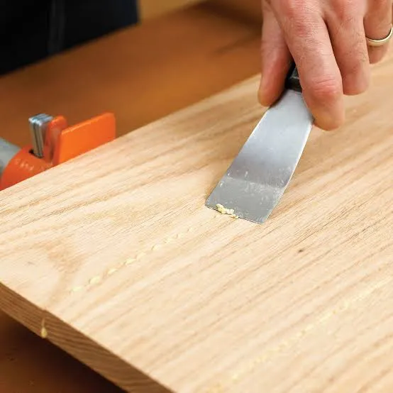 woodworker cleaning thick glue lines and squeeze out residue from panel surface using a scraper